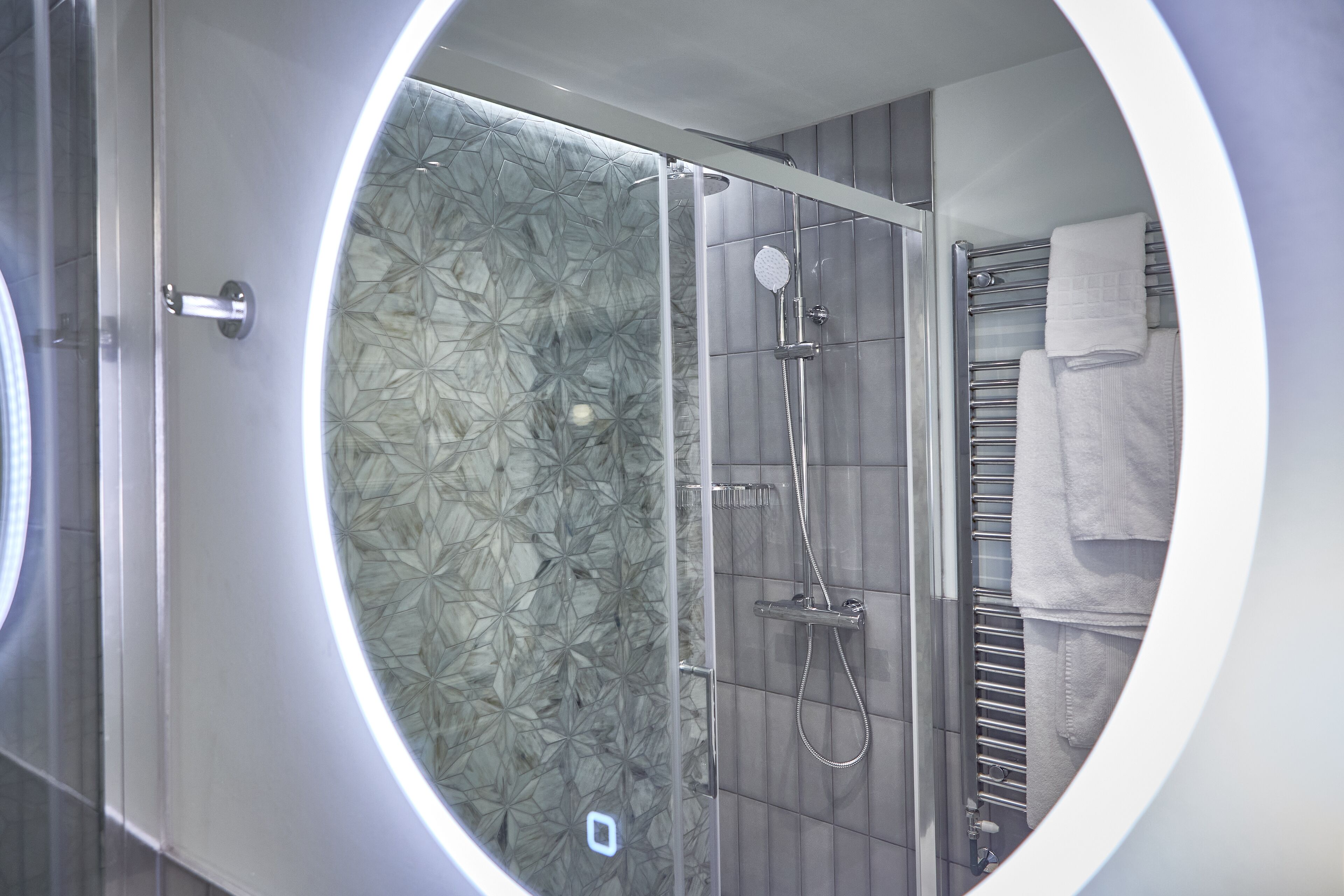 A modern bathroom with a glass-enclosed shower, a towel rack, and a circular mirror.