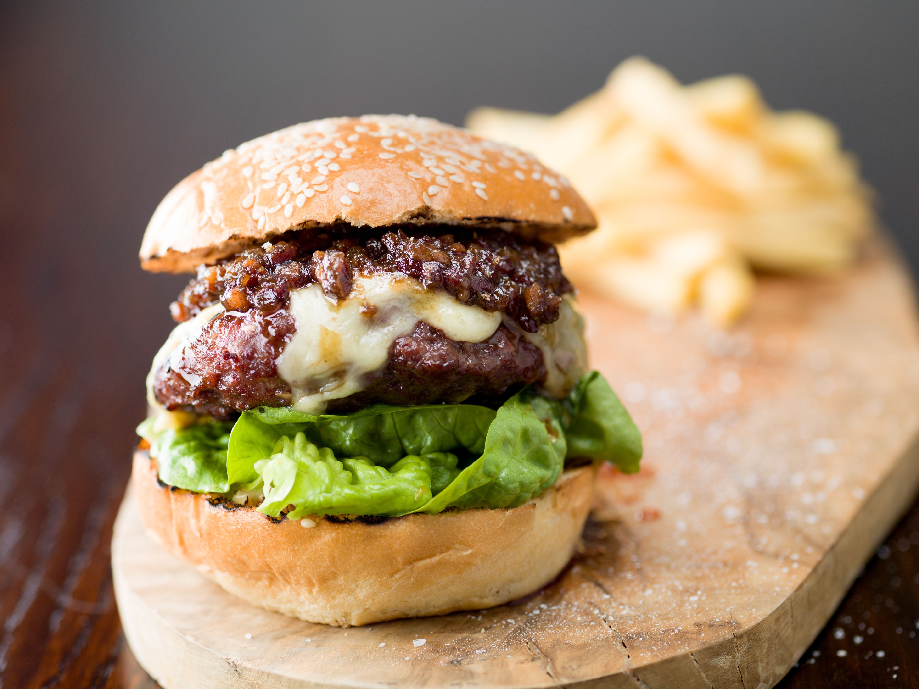 A burger with lettuce and cheese on a bun, accompanied by fries on a wooden board.