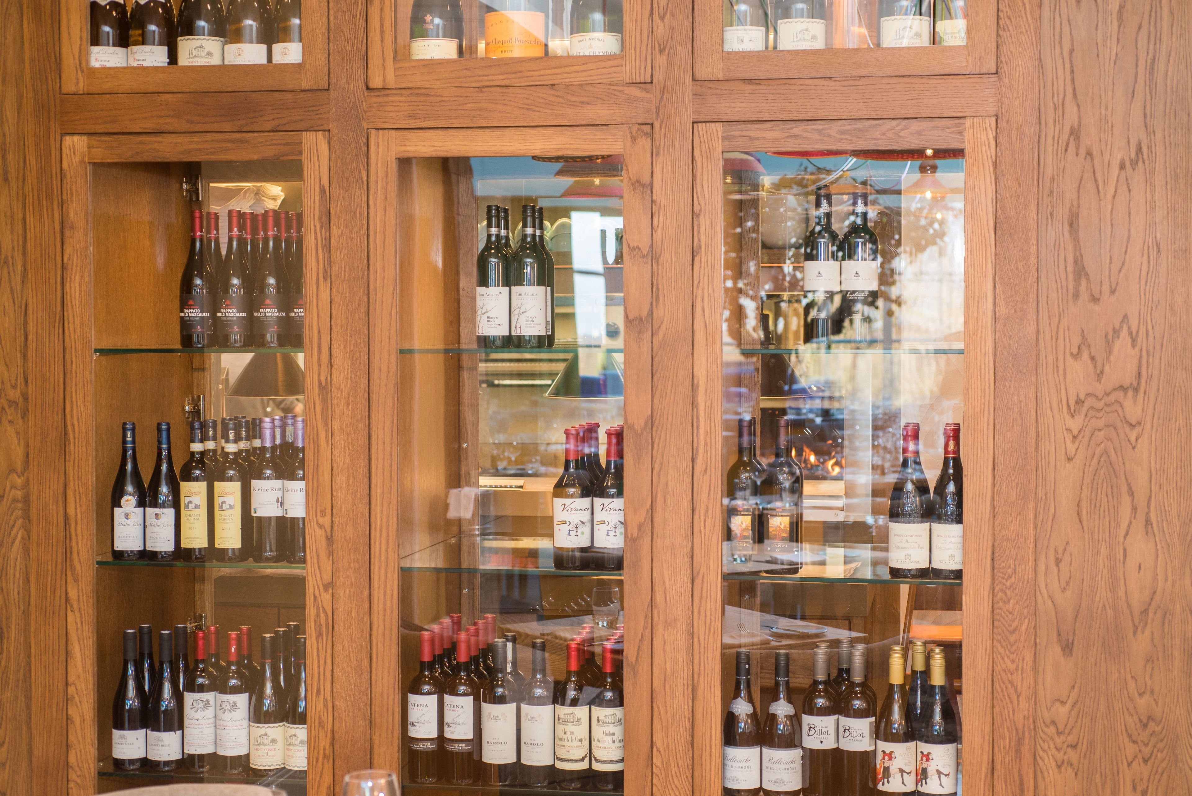 A wine cellar with wooden shelves and glass doors displaying various wine bottles.