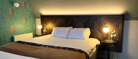 A hotel room with a large bed, two bedside tables with lamps, a headboard, and a wall with a leaf pattern.