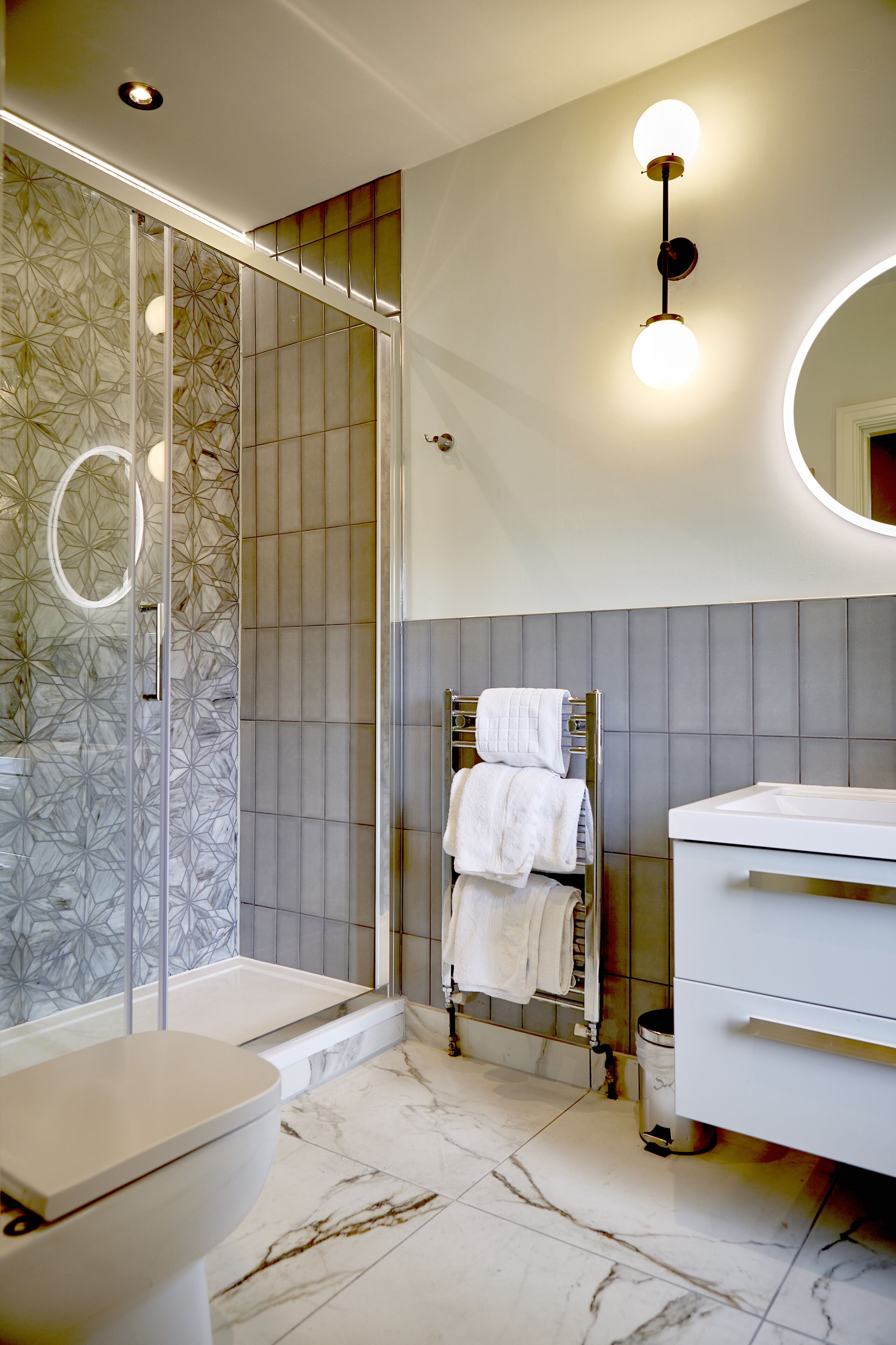 Un baño moderno con cabina de ducha de vidrio, inodoro blanco, tocador con espejo y barra para toallas.