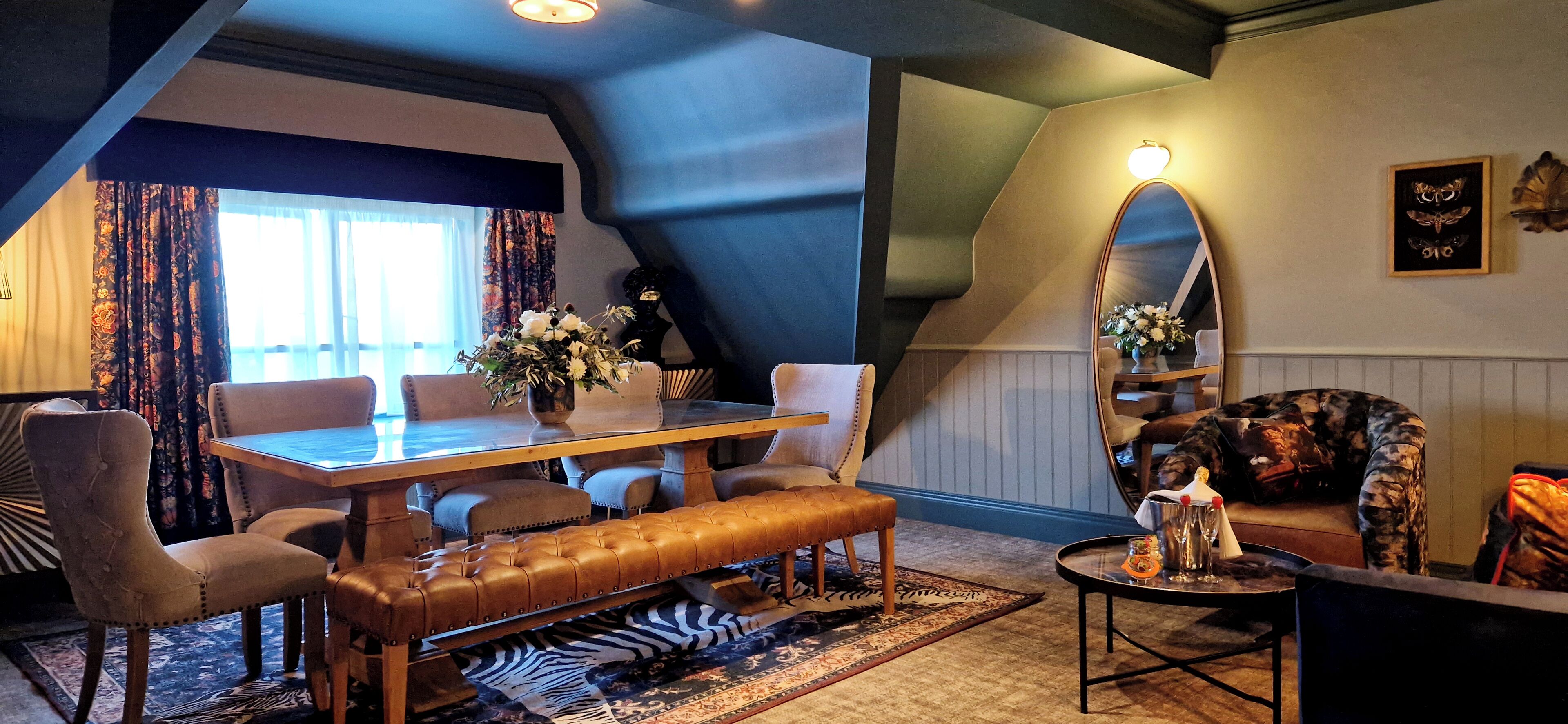 A cozy room with a wooden dining table, leather bench, and a large mirror.