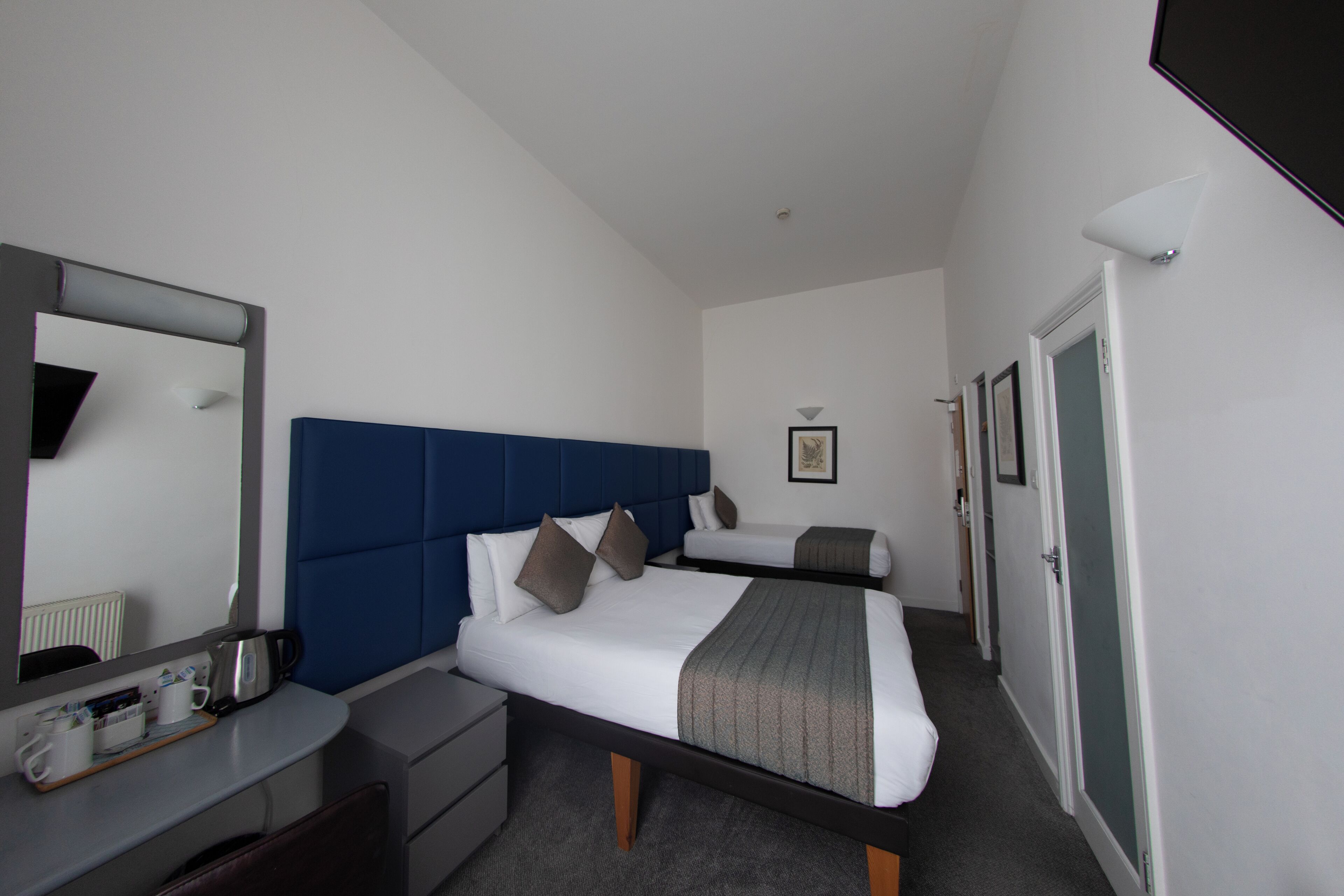 Una habitación de hotel con una cama grande, una mesita de noche, un aparador, un espejo y una puerta.