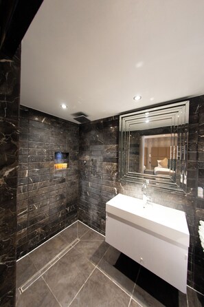 A modern bathroom with dark marble walls, a white sink, and a large mirror. - Duke of Leinster (London)
