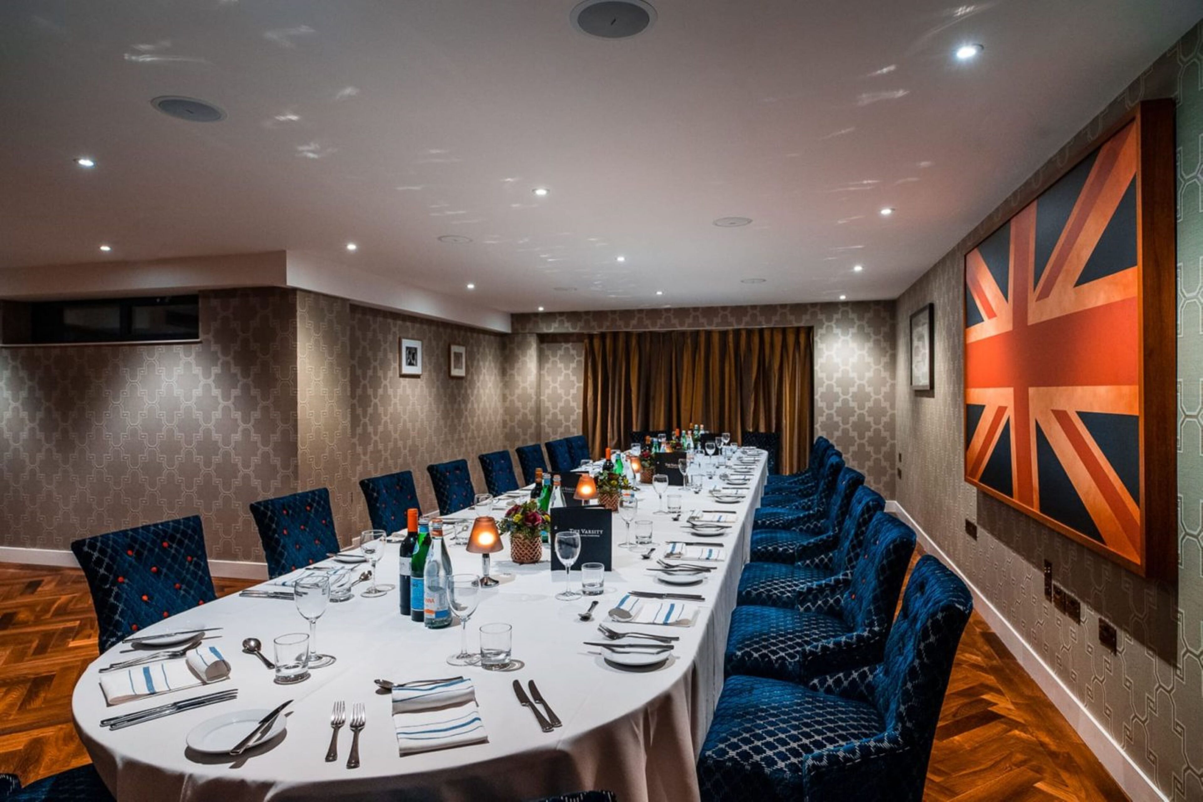Una sala de conferencias con una larga mesa dispuesta para una reunión, sillas tapizadas en azul y una gran decoración de la bandera Union Jack en la pared.