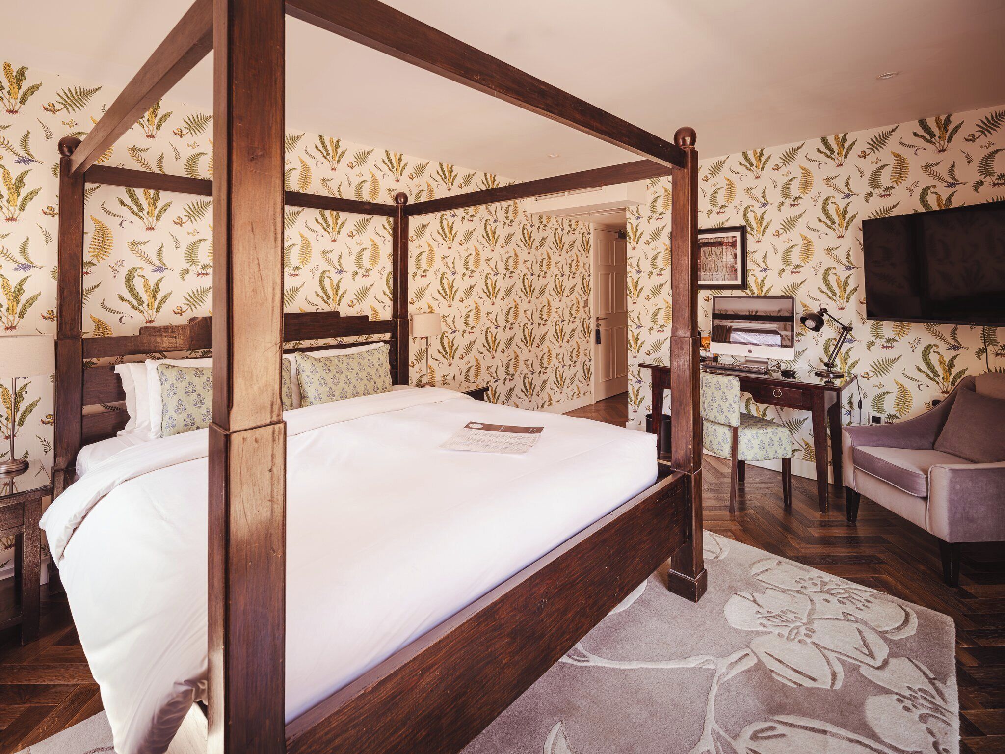 A four-poster bed with a wooden frame, a desk with a computer, a chair, and a television.