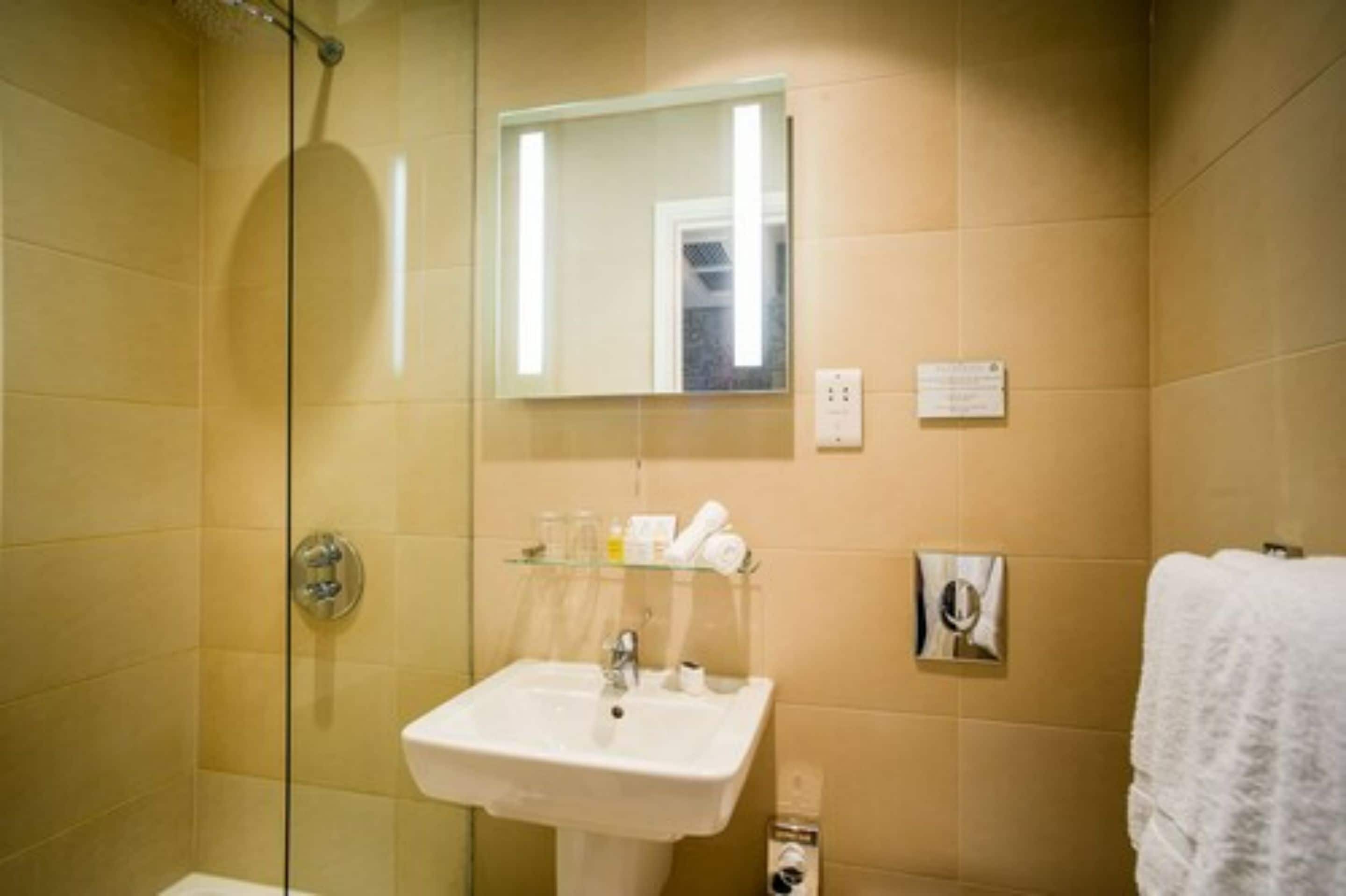 A bathroom with a glass shower enclosure, a white sink, a mirror, and a towel rack.