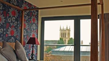 A bedroom with a large bed, floral wallpaper, and a view of a historic building.