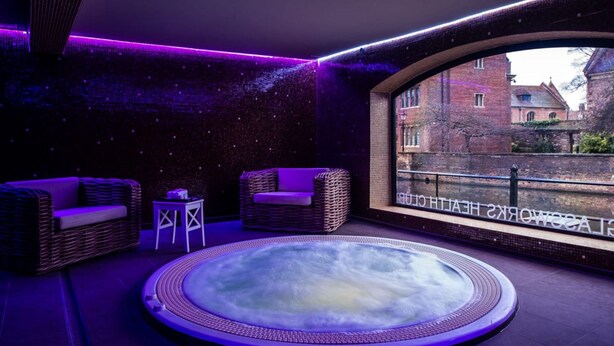 A spa room with a hot tub, wicker furniture, and a view of a historic building. - The Varsity Hotel & Spa (Cambridge)