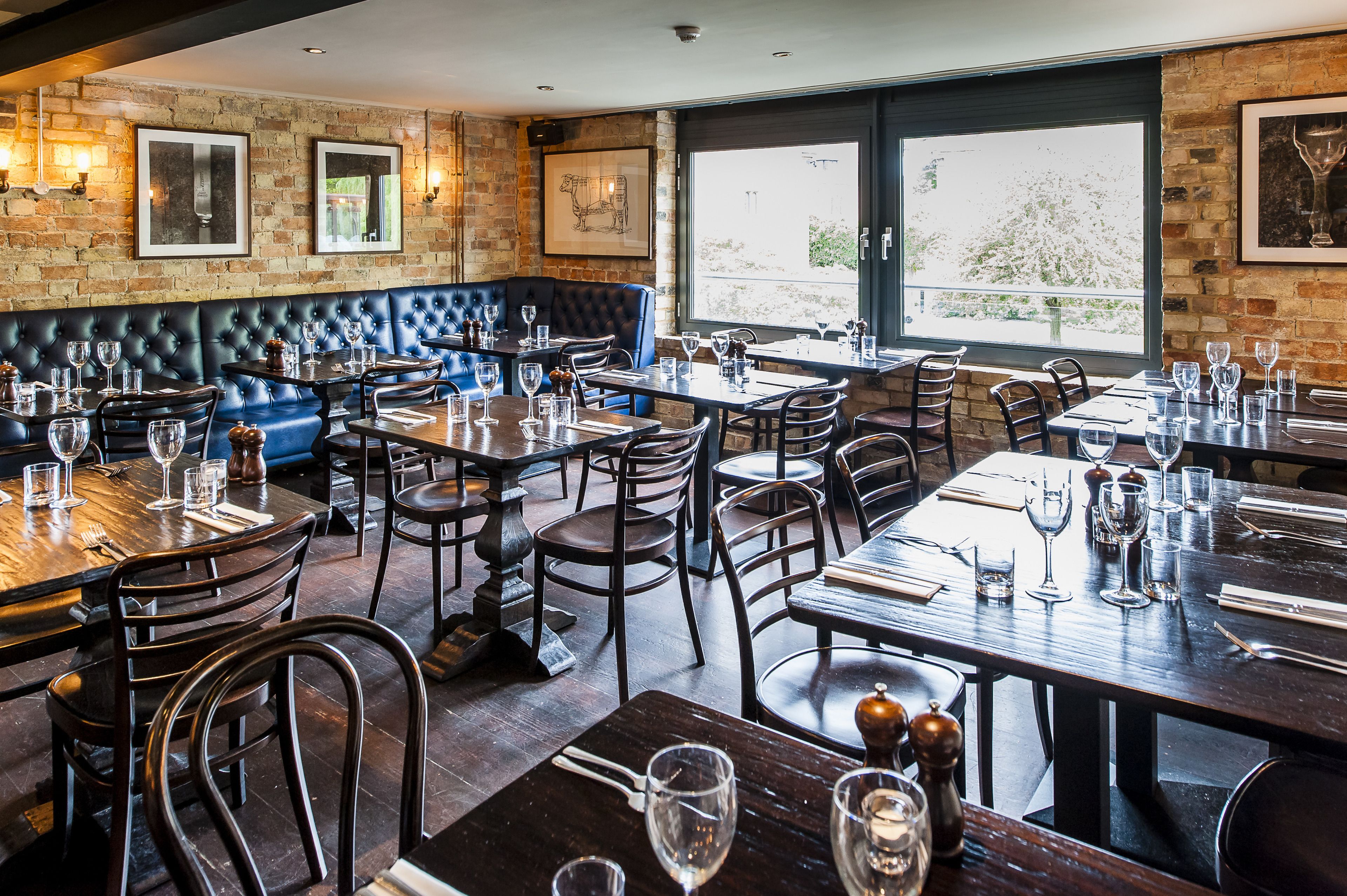 A restaurant with brick walls, leather booths, and wooden tables set for dining.