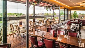 A restaurant with wooden tables and red upholstered chairs, large windows with a city view, and hanging flower arrangements. - The Varsity Hotel & Spa (Cambridge)