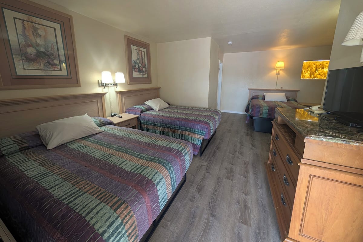 A hotel room with two beds, a desk, a dresser, and a television.