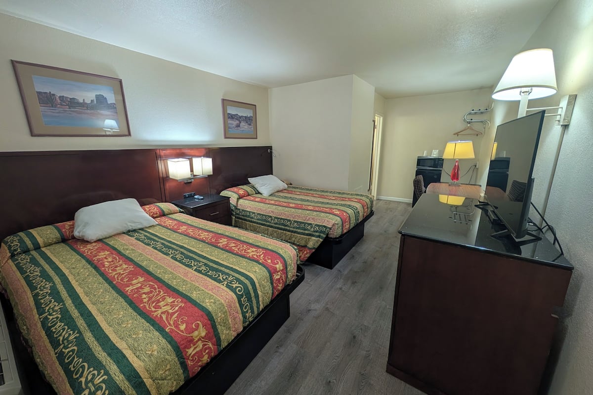 A hotel room with two beds, a desk, a mirror, and a TV.