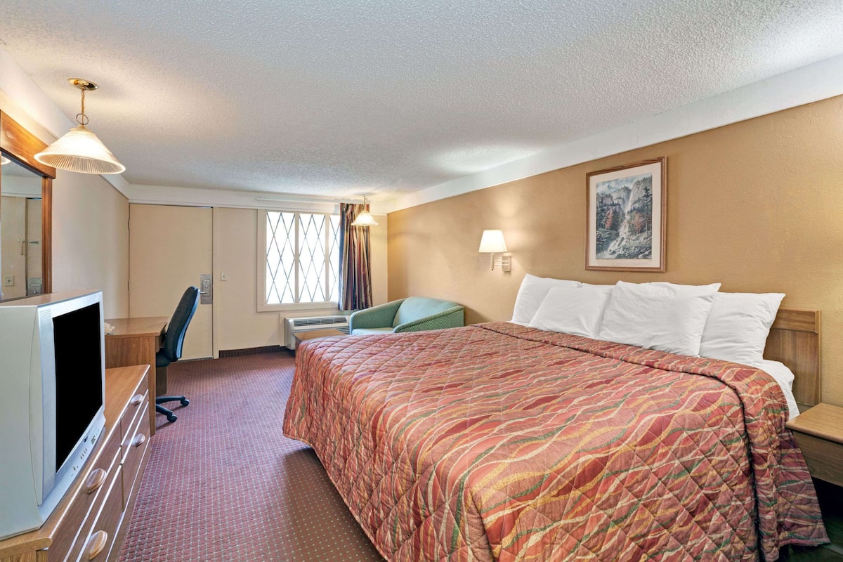A hotel room with a large bed, a desk with a computer, a chair, and a window with curtains.