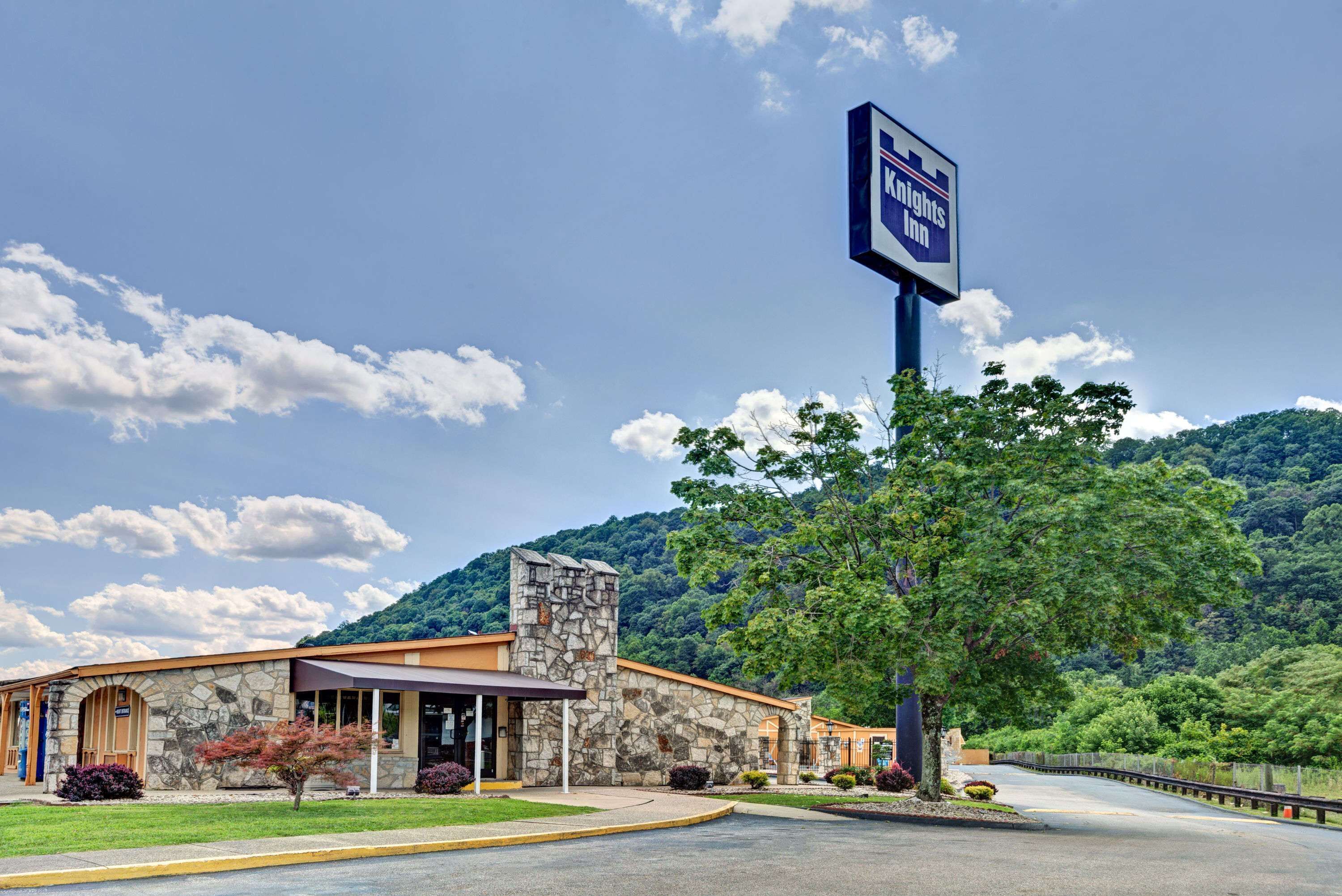 A stone building with a large sign for Knights Inn, surrounded by greenery and hills.