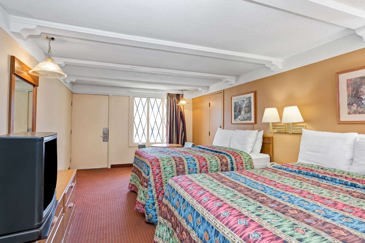 A hotel room with two beds, a television, a window with curtains, and a painting on the wall.