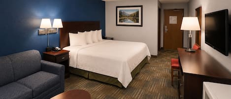 A hotel room with a bed, a sofa, a desk, a television, and a painting on the wall.