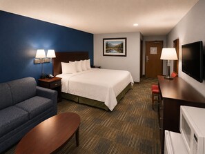 A hotel room with a bed, a sofa, a desk, a television, and a painting on the wall. - Corning Inn (Painted Post)