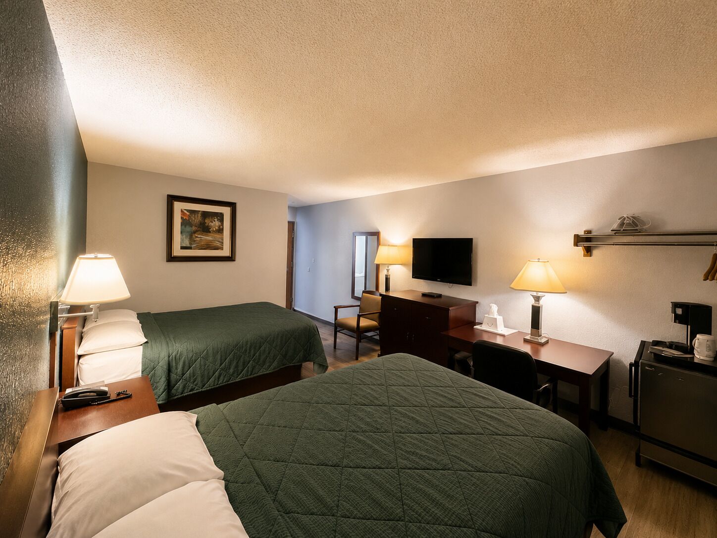 A hotel room with two beds, a desk, a chair, a television, and a coffee machine.