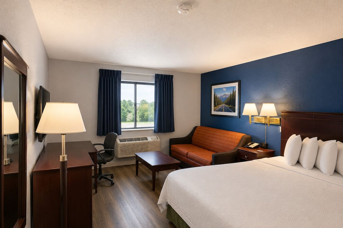 A hotel room with a bed, desk, chair, and a window with curtains.