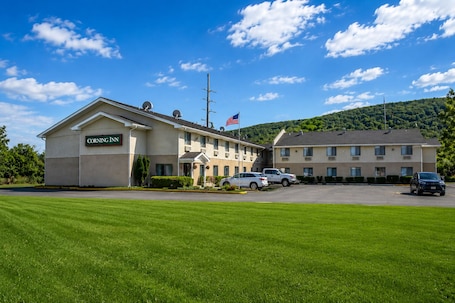 A hotel with a sign reading 'CORNING INN,' a parking lot with several cars, and a mountainous backdrop.. Corning Inn