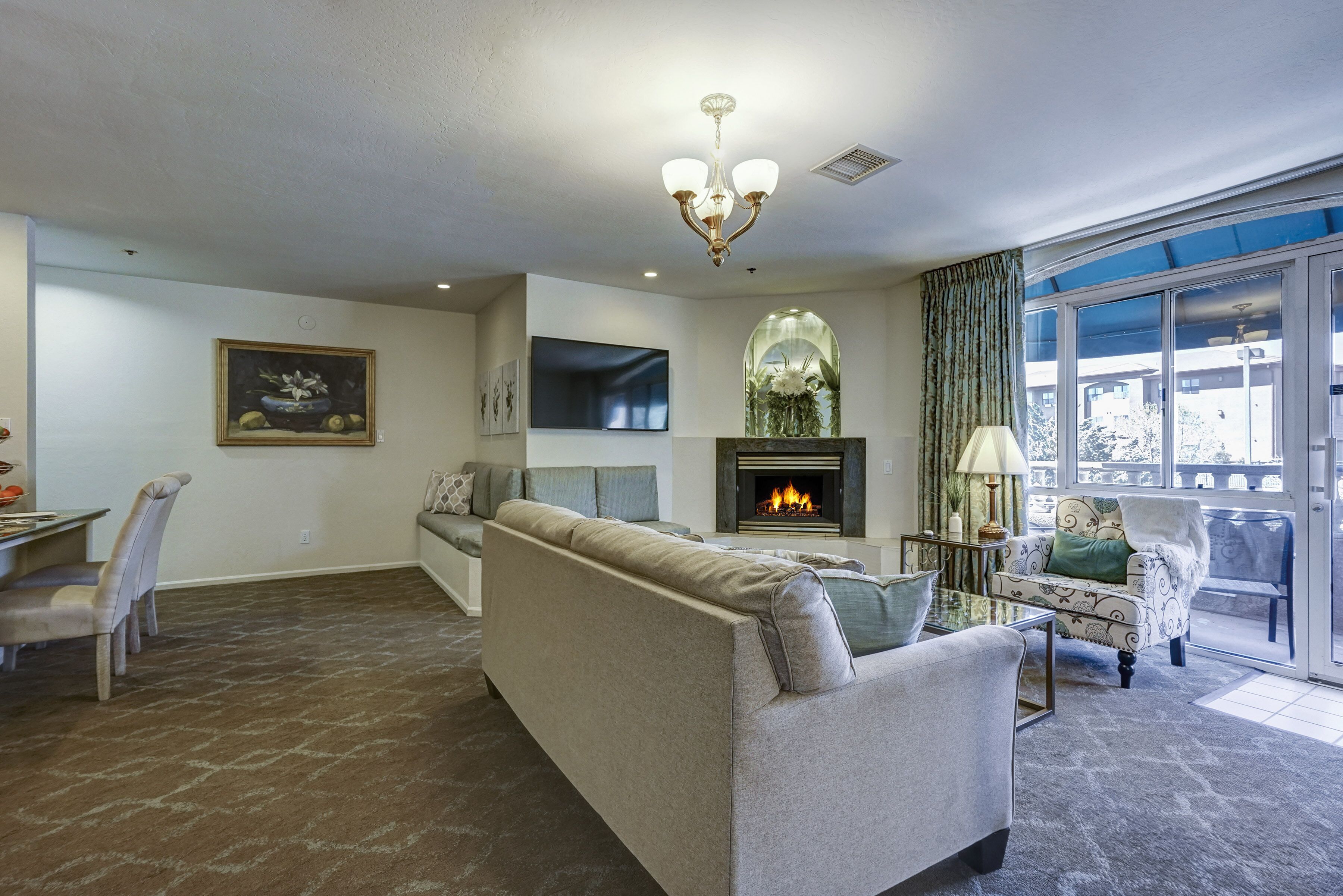 A living room with a sofa, a fireplace, a dining area with chairs, and a large window with curtains.