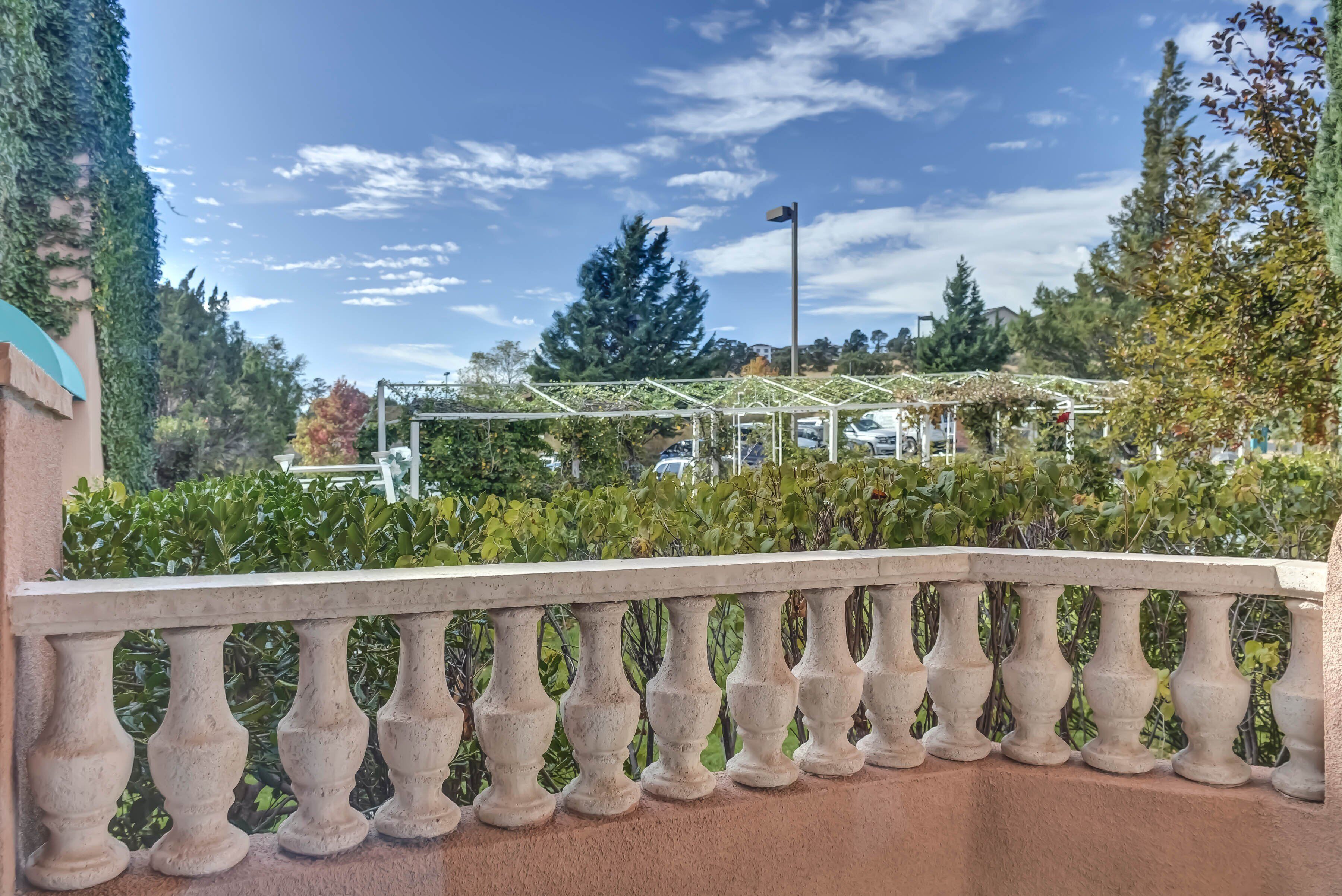 Un balcón con barandilla de hierro forjado que da a un jardín con una estructura de pérgola.