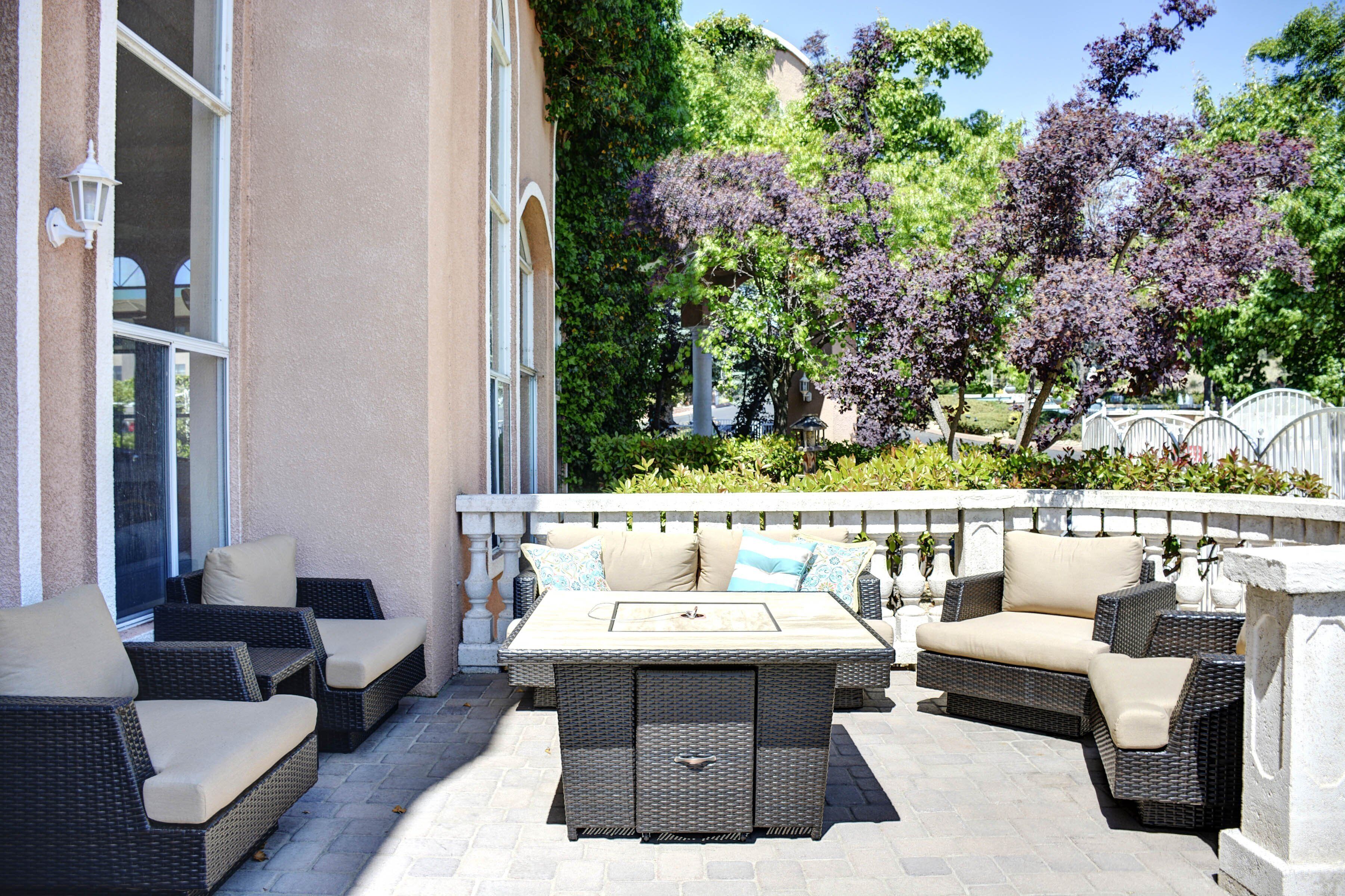 Un patio al aire libre con mobiliario de mimbre, una mesa y vistas a árboles y un edificio.