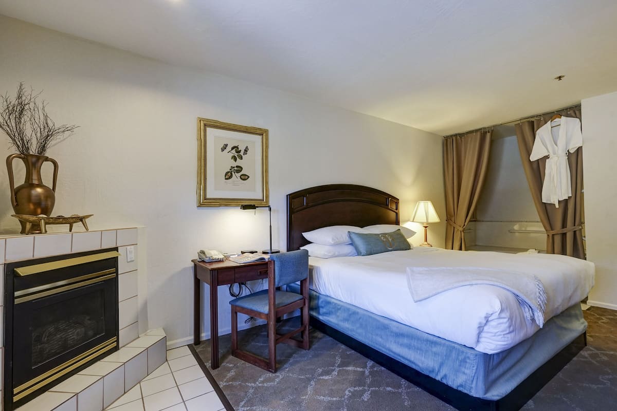 Ein Hotelzimmer mit Bett, Schreibtisch mit Stuhl, Kamin und botanischem Druck im Rahmen an der Wand.