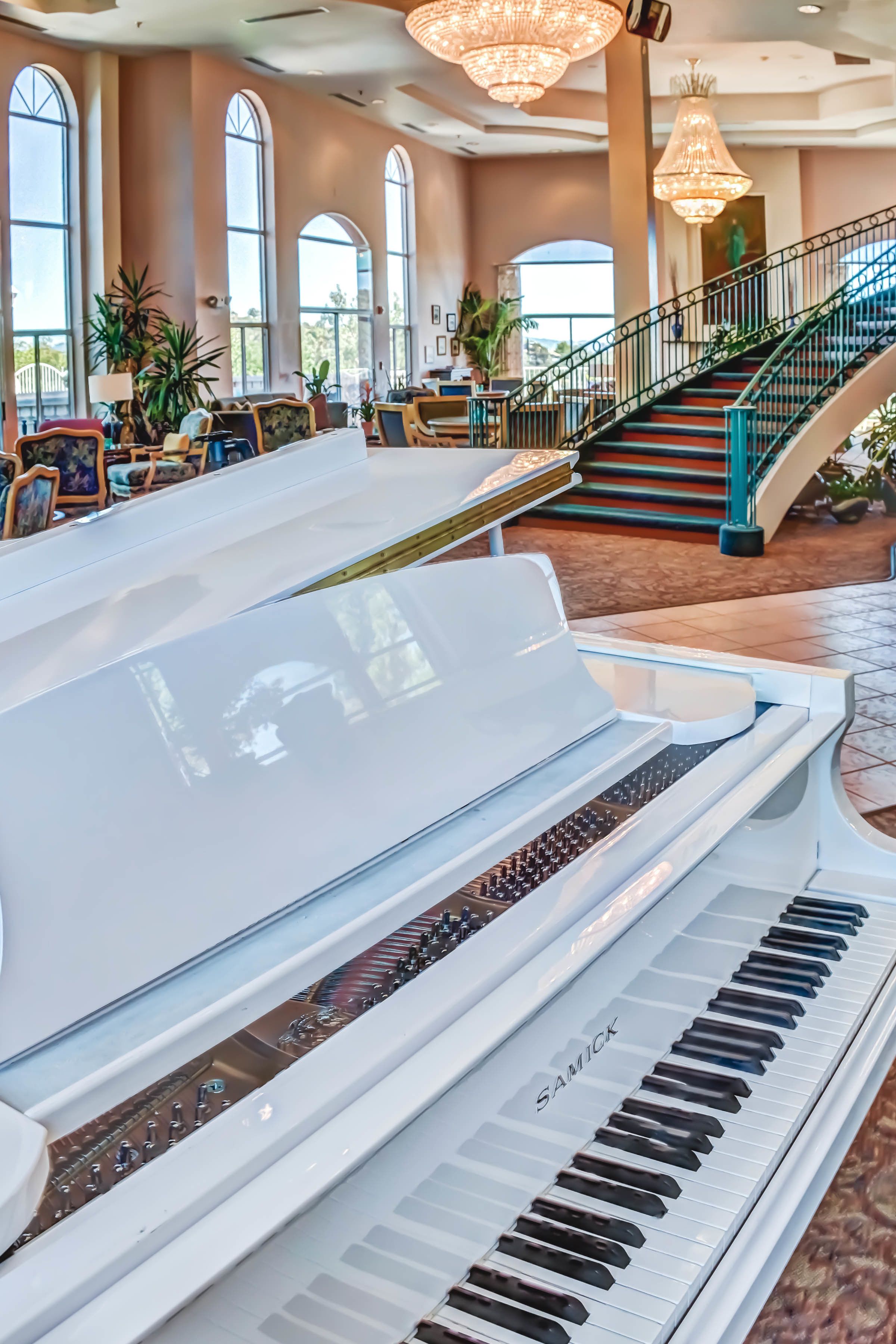 A grand piano in a spacious lobby with large windows, a staircase, and comfortable seating areas.