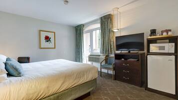 Een hotelkamer met een bed, een bureau met een televisie, een magnetron en een koelkast.