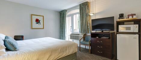 A hotel room with a bed, a desk with a television, a microwave, and a refrigerator.