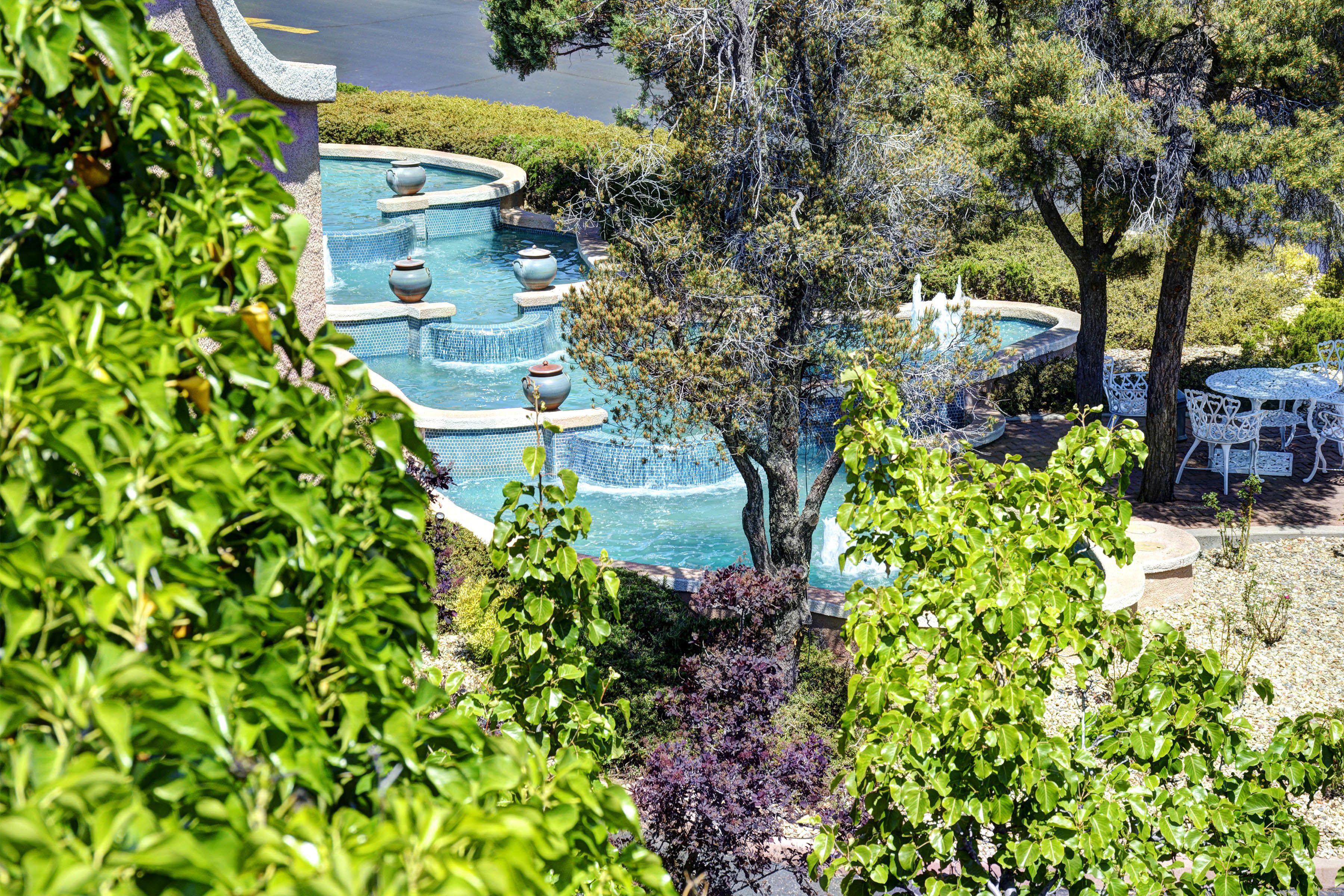 A multi-tiered swimming pool with tiered steps and decorative vases, surrounded by lush greenery and trees.