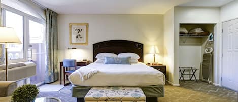 A hotel room with a large bed, a bedside table, a chair, a small table with a plant, and a view of the outside through a window.