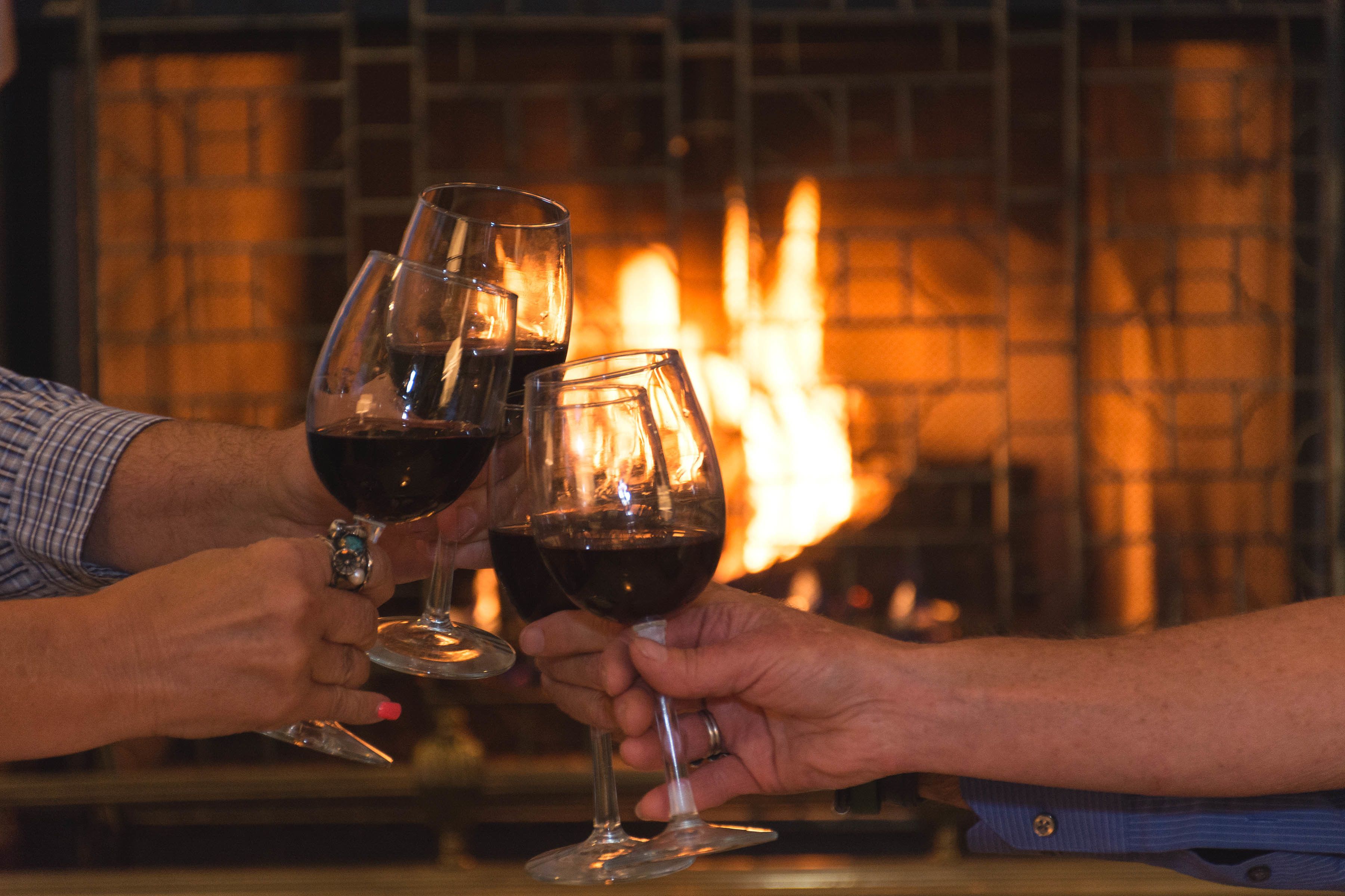 Two people holding wine glasses in front of a fireplace.