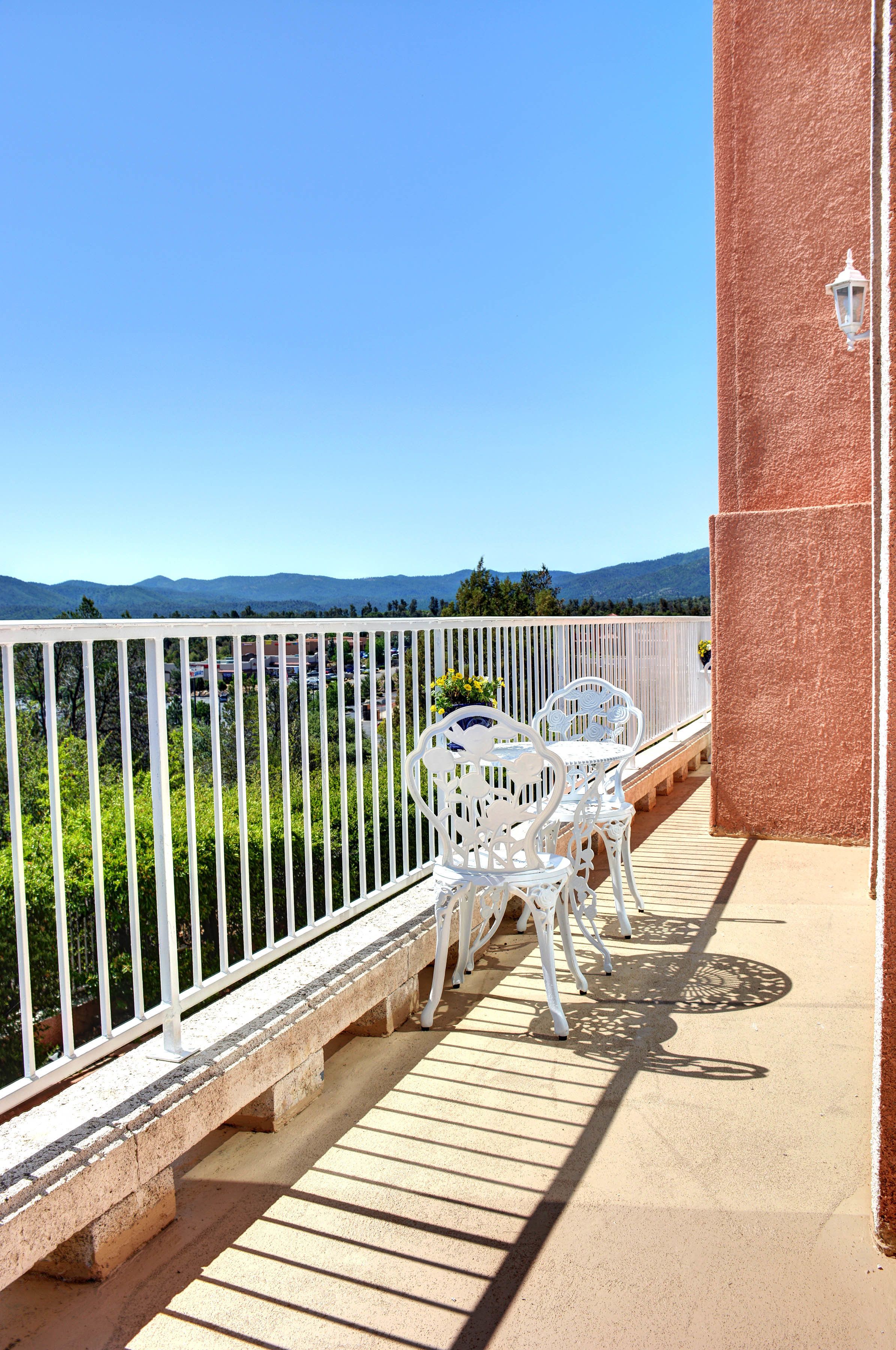 Un balcon avec des balustrades en métal blanc, une table avec des chaises et une vue sur les montagnes au loin.