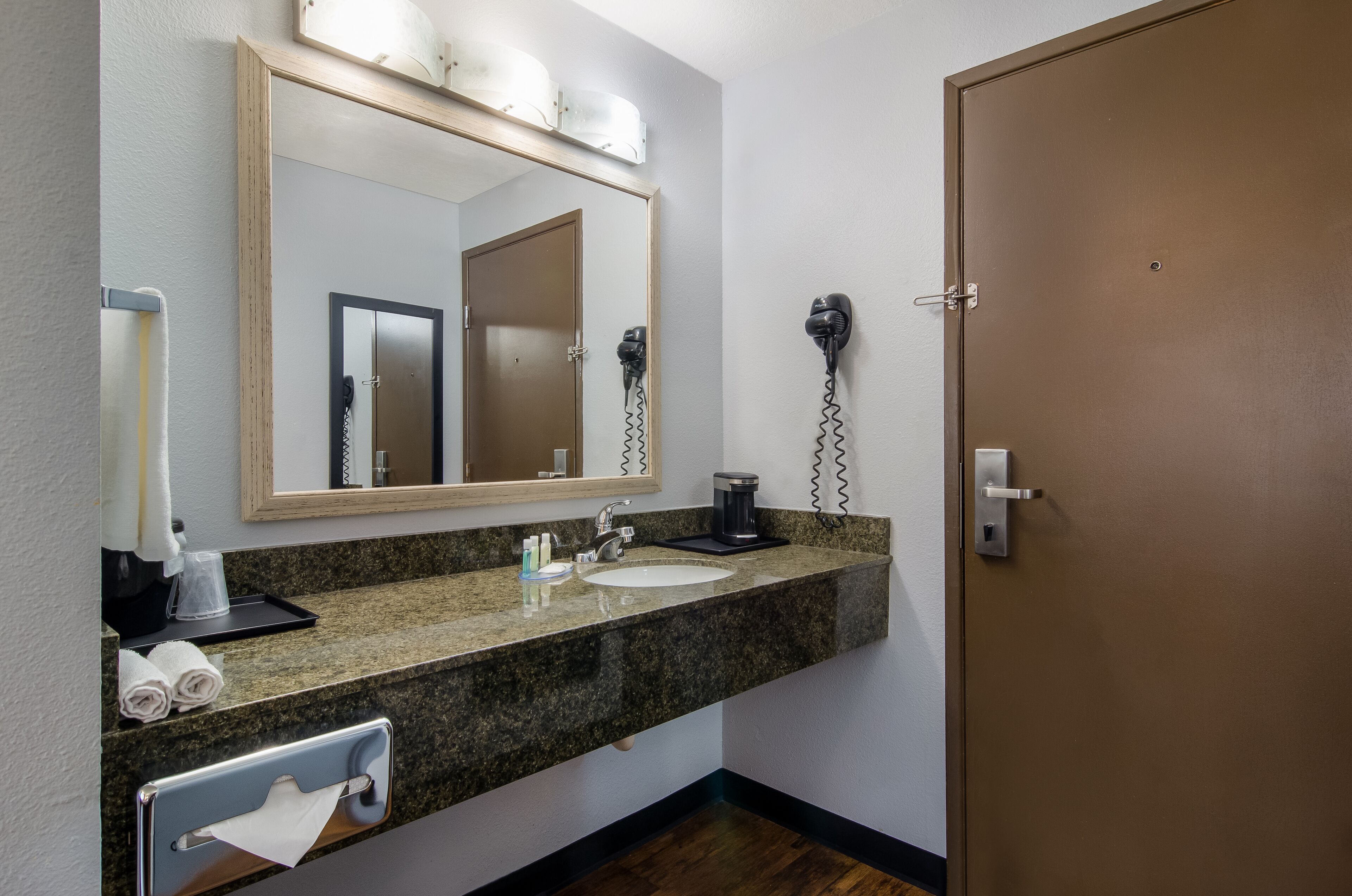 A bathroom with a granite countertop, a sink, a mirror, a hairdryer, and a door.