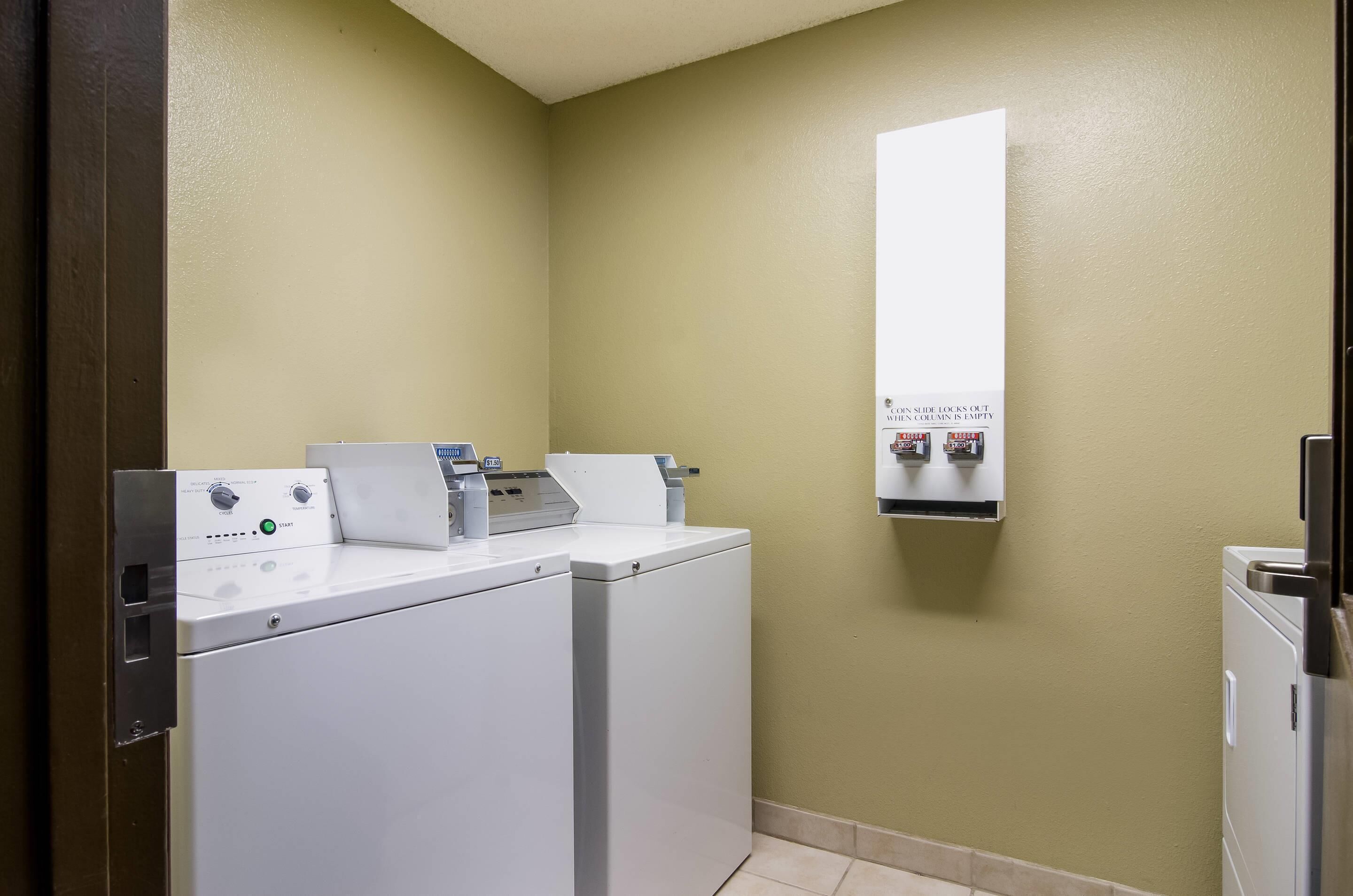 A laundry area with two washing machines, a dryer, and a wall-mounted dispenser.