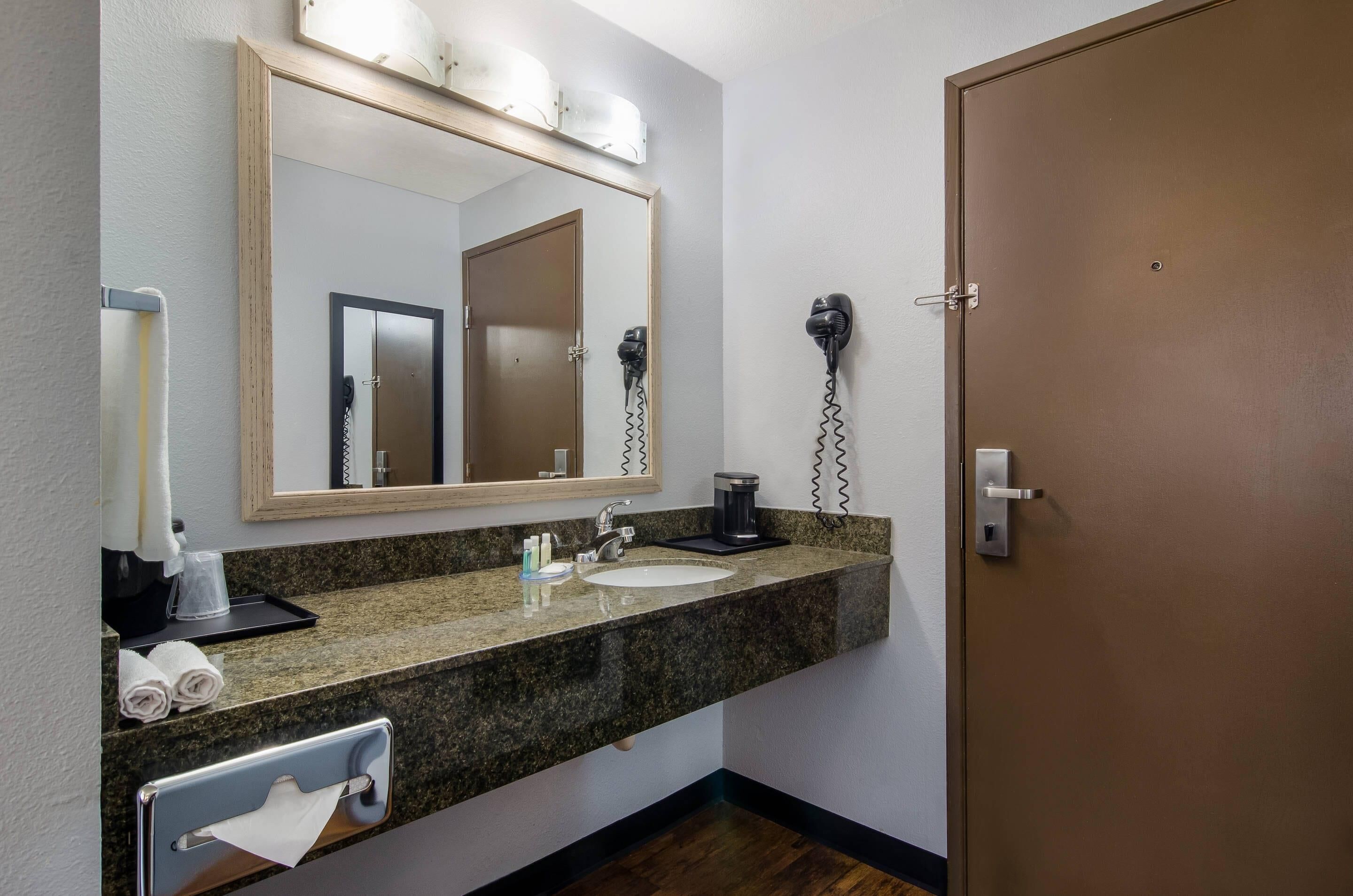 Uma casa de banho com bancada de granito, lavatório, espelho, secador de cabelo e porta.