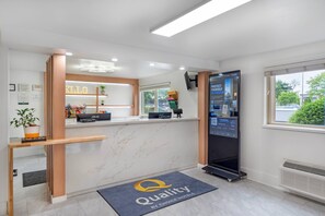 A hotel reception area with a digital information board, a reception desk, and a 'Quality' doormat. - Quality Inn & Suites Silverdale Bangor - Keyport (Silverdale)