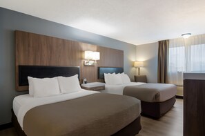 A hotel room with two beds, a wooden headboard, bedside lamps, and a large window with curtains.