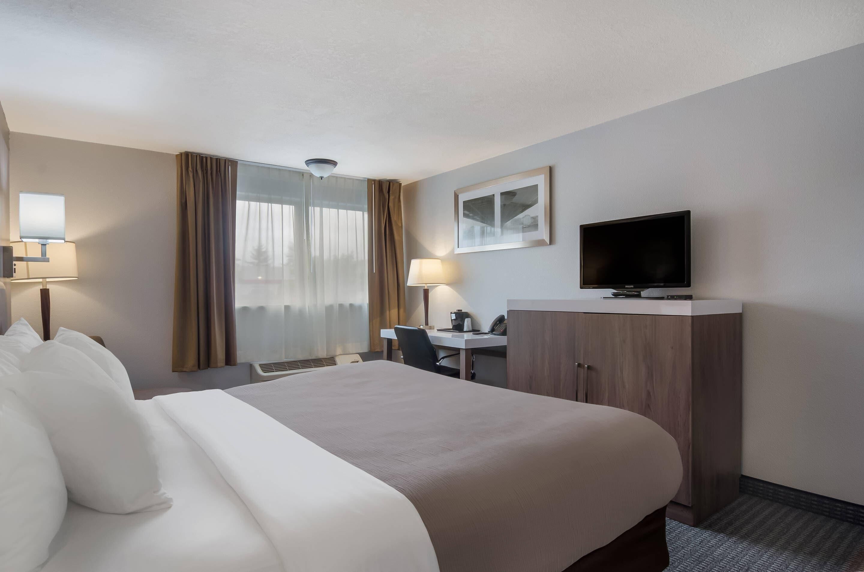 A hotel room with a bed, desk, television, and a window with curtains.