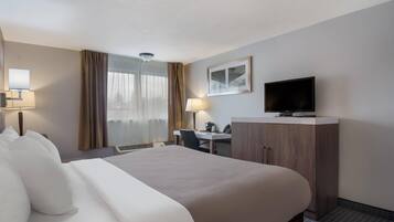 A hotel room with a bed, desk, television, and a window with curtains.