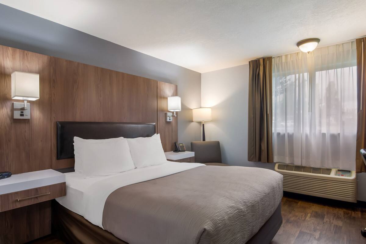 A hotel room with a large bed, wooden headboard, bedside lamps, a desk, and a window with curtains.