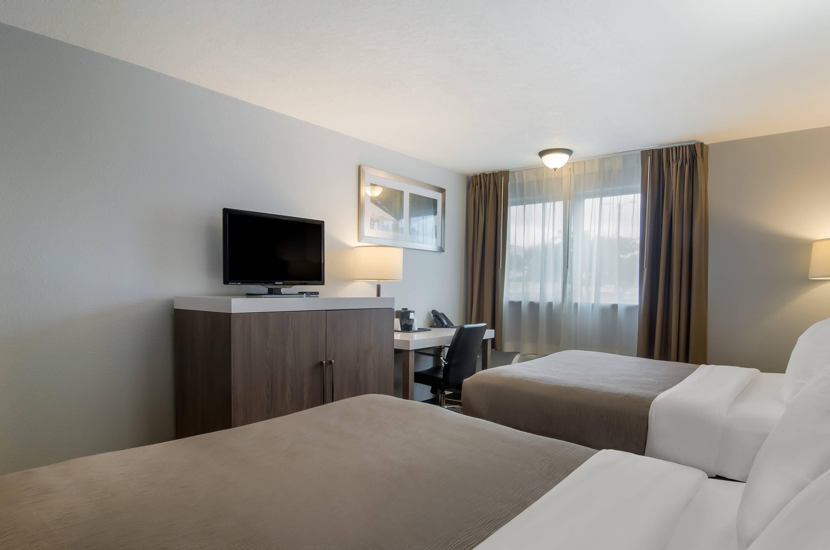 A hotel room with two beds, a desk, a television, and a window with curtains.