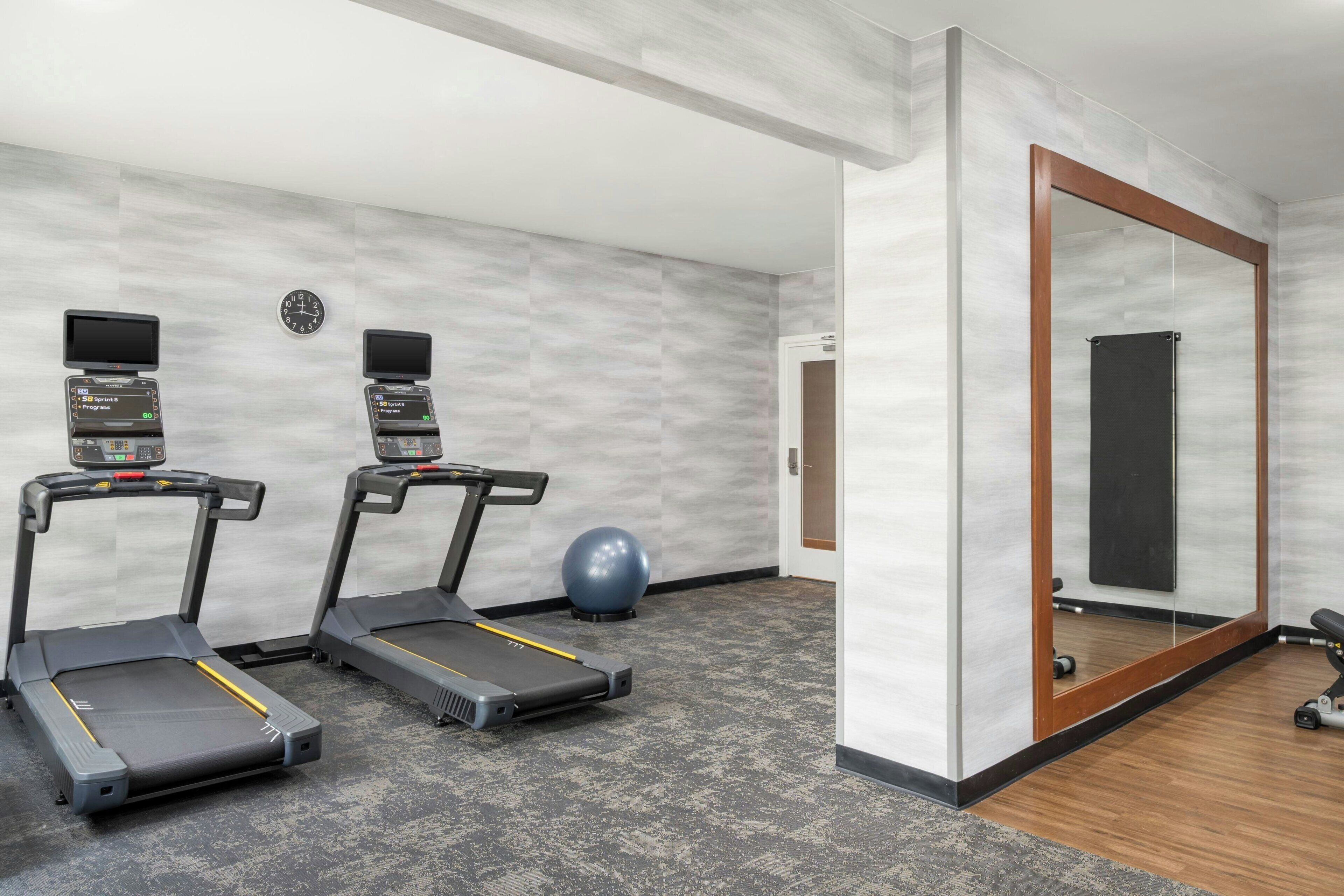 Gimnasio con cintas de correr, bicicleta estática, un reloj de pared y un espejo grande.