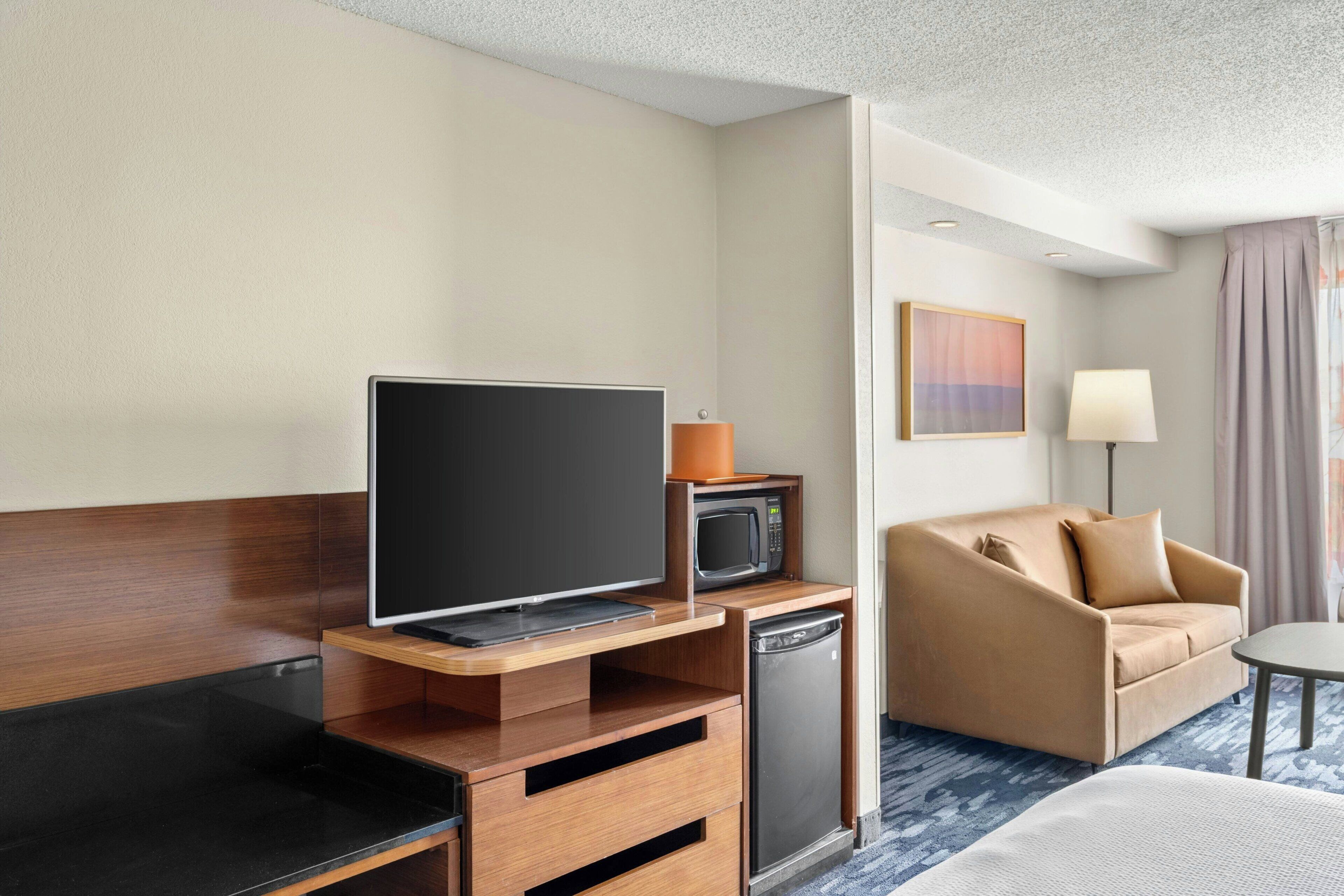 A hotel room with a flat-screen TV, a microwave, a small refrigerator, a sofa, and a bedside table.