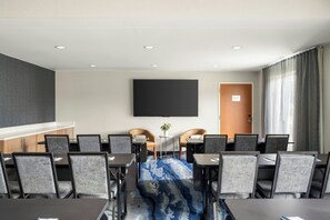 Une salle de conférence dotée d’un grand téléviseur à écran plat fixé au mur, d’une porte portant l’inscription « Local des équipements d’ascenseur » et d’un tapis bleu à motifs.