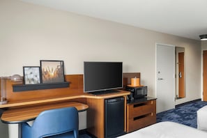 Une chambre d’hôtel équipée d’un lit, d’un bureau avec un ordinateur, d’une télévision, d’un four à micro-ondes et d’un petit réfrigérateur.