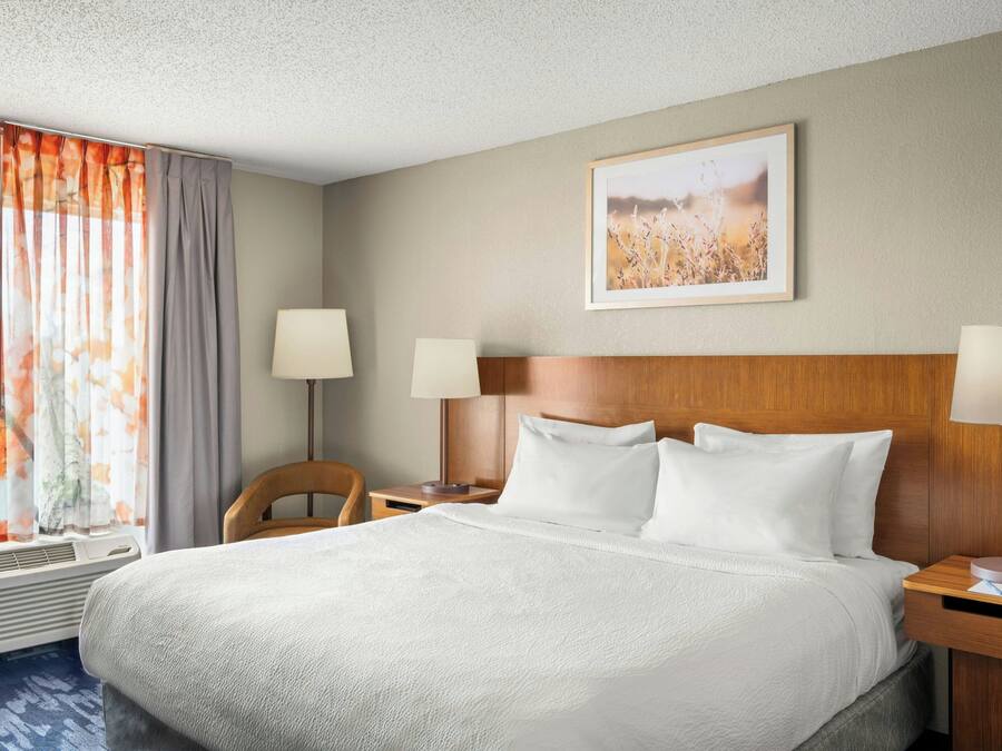 Una camera d'albergo con un letto grande, due comodini con lampade, una finestra con tende e un quadro appeso al muro.